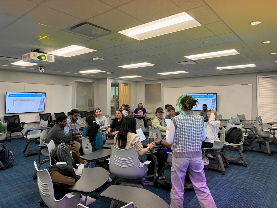 Students sit at desks in a genomics class while one stands in front of the group.