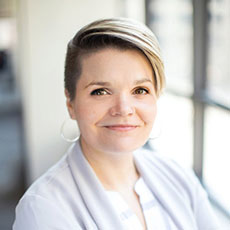 Katie Heiden Rootes headshot. Katie Heiden Rootes, headshot. She is looking at the camera while wearing a grey sweater and light blouse.