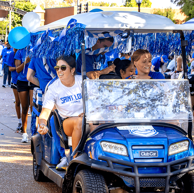 Students ride in a parade on decorated golf carts, throwing candy toward the crowd.