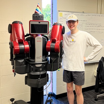 Pascal Sikorski Photo Pascal Sikorski staning next to and smiling with a robot in the Mecharithm Lab.