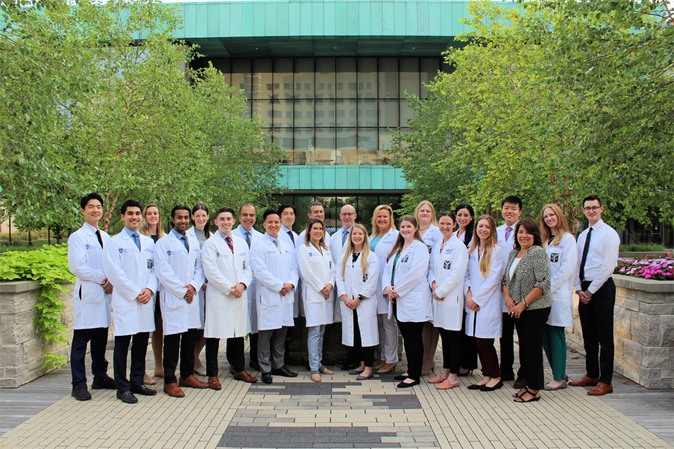 Faculty, Staff, and Residents- Class of 2023-2024 More than 20 faculty, staff and residents stand in two rows outside of a building on the SLU campus.