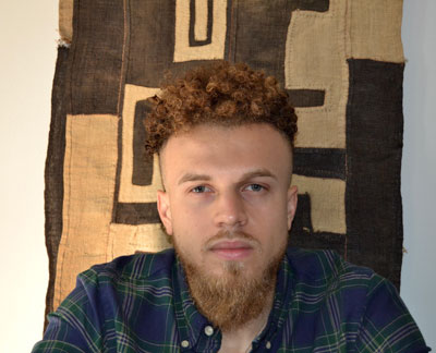 Bentley Brown Art historian Bentley Brown gazes directly at the viewer while sitting in front of a brown and beige swath of fabric with an abstract design.