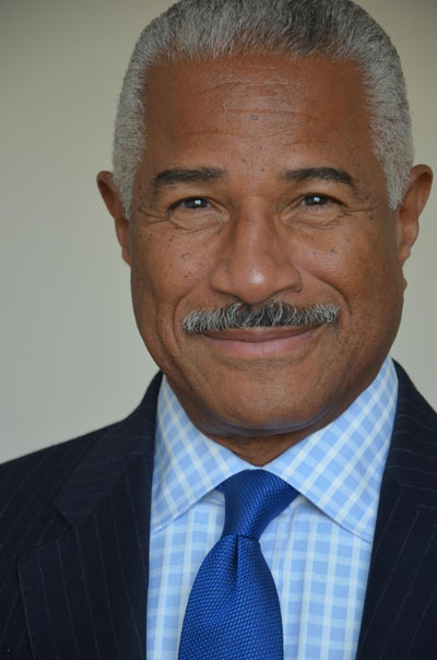 Felipe Luciano A close-up photo of poet and activist Felipe Luciano, dressed in pale blue-and-white checkered shirt, cobalt blue tie and navy blue pinstripe jacket