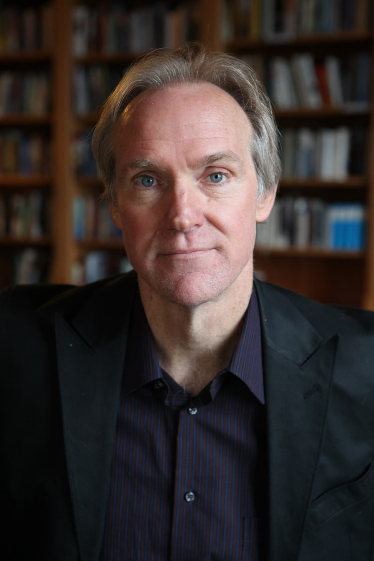 Tom Sleigh Poet Tom Sleigh sits in a library room with books on shelves behind him