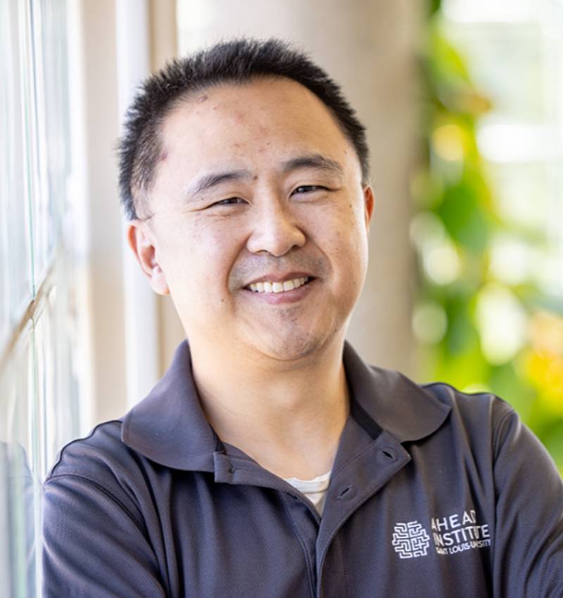 A man poses for a photo indoors next to a window. He smiles for the camera.