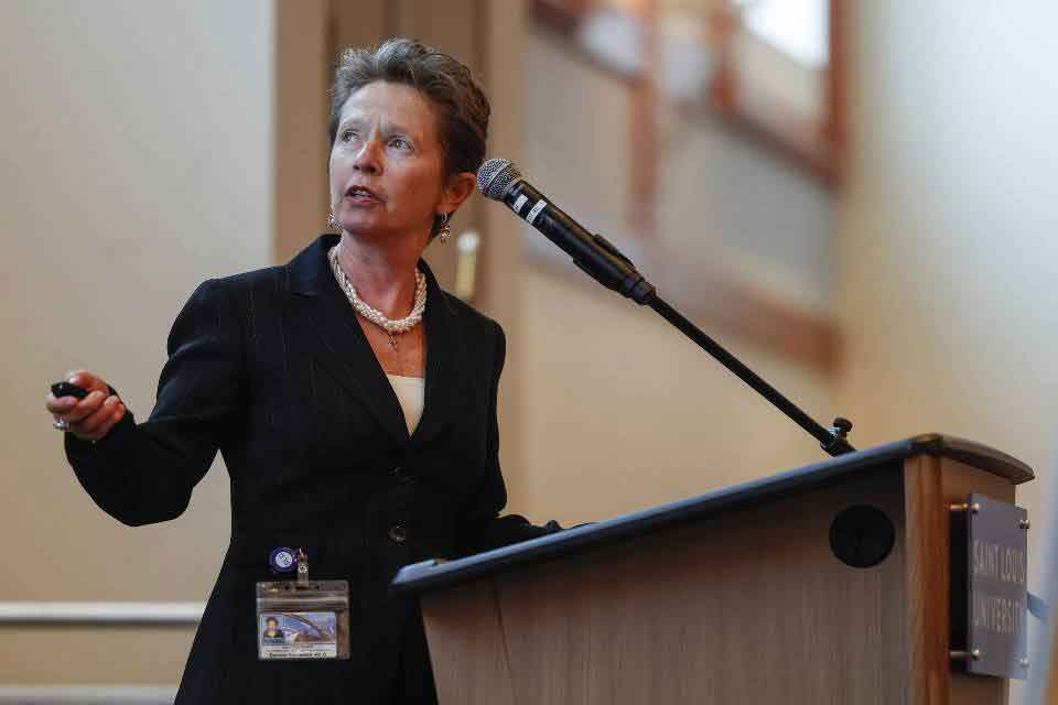 A woman stands behind a podium, presenting data on a projector screen off-camera to a crowd of attendees at SLU’s annual Neuroday event
